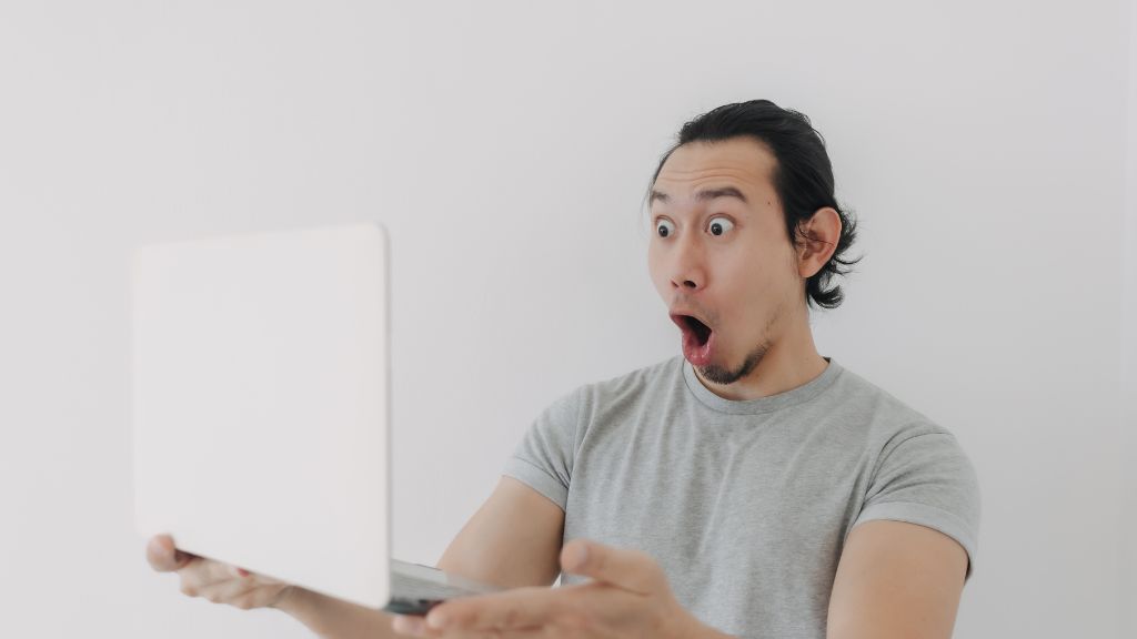 A man holding his laptop looks shocked and thrilled after discovering he was approved for a New Jersey cannabis license, representing success made possible through understanding New Jersey cannabis laws and expert cannabis consulting.