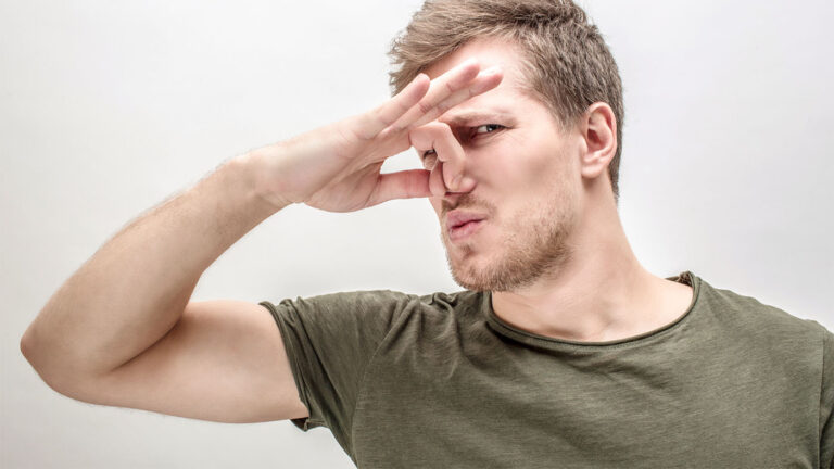Person holding their nose due to strong cannabis odor outside a greenhouse.