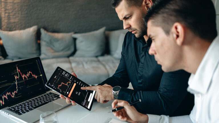 Two men reviewing financial data on a tablet, discussing Funding for Cannabis Businesses, Cannabis Startup Costs, and a Cannabis Profitability Strategy.