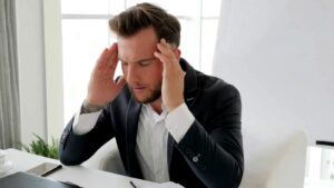 Professional overwhelmed by cannabis startup costs, sitting at desk reviewing cannabis facility build-out expenses and working capital needs.