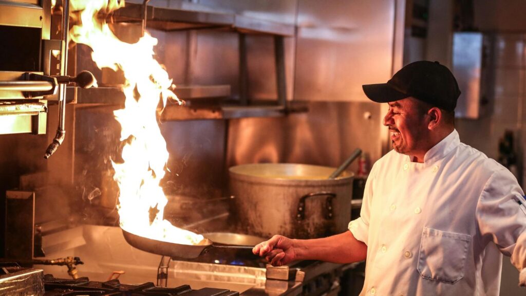 A chef igniting a tall flame in a commercial kitchen represents the passion, precision, and performance needed to create top-tier dispensary operations and an exceptional cannabis customer experience.