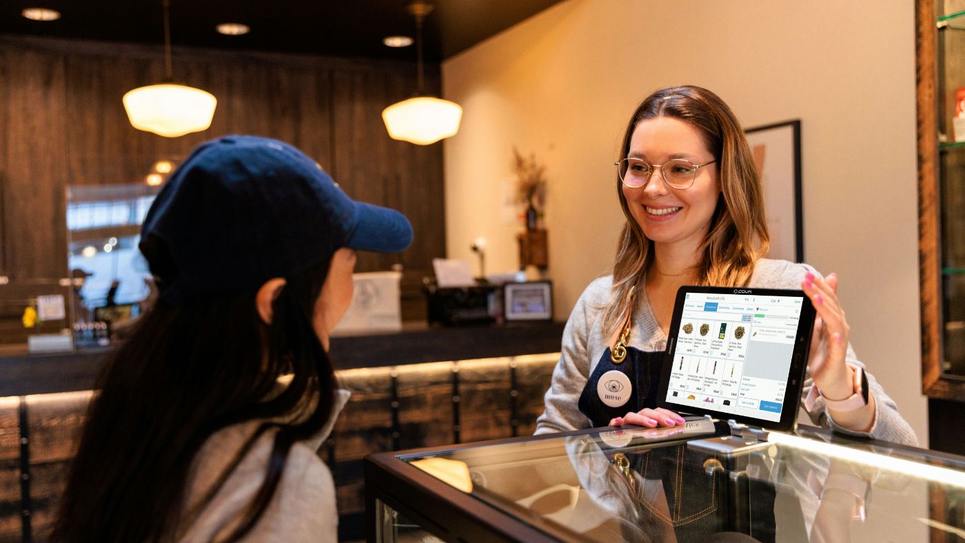 Dispensary customer checking out with a budtender at a POS terminal. Use the Dispensary Profit Projector to create your Cannabis Business Plan.