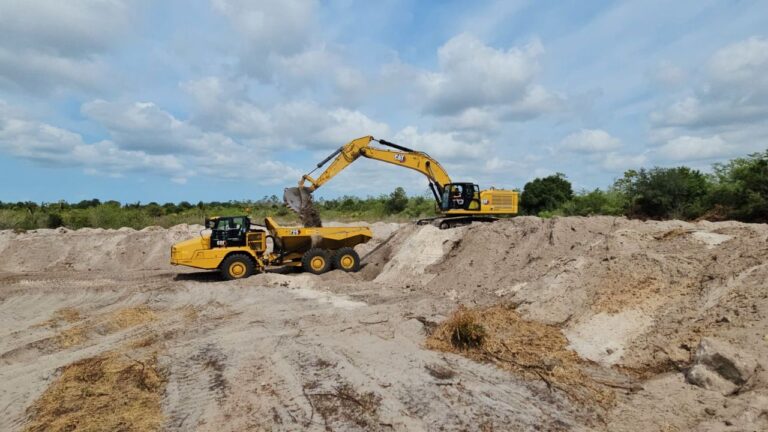 A Bobcat excavator and dump trucks preparing the ground for a large-scale cannabis cultivation facility.